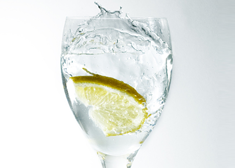 Ett högt glas på fot med citronskiva och vatten som splashar.