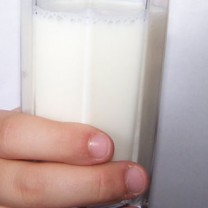 En hand håller ett välfyllt glas mjölk