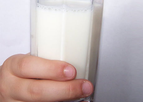 En hand håller ett välfyllt glas mjölk