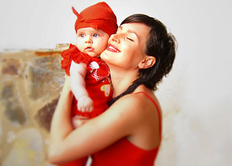 Mörkhårig kvinna i röd topp håller sin bebis kind mot kind