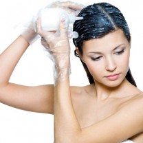 Mörkhårig kvinna står i handduk och applicerar hårfärg i håret