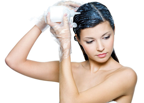 Mörkhårig kvinna står i handduk och applicerar hårfärg i håret