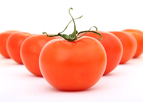 Tomater ligger uppradade i en triangel på vitt bord