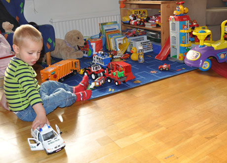 Liten pojke sitter och leker med en polisbil i sitt lekrum fullt av leksaker i olika material