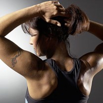 Mörkhårig muskulös kvinna i träningskläder sträcker på sig i profil