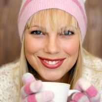 Leende vacker blond kvinna i vinterkläder rosa mössa och vantar håller i kaffekopp