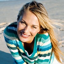 Leende blond tjej sitter på sandstrand i randig tröja