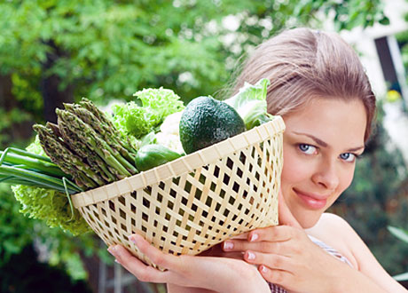 Vacker kvinna håller korg med grönsaker över axeln