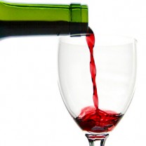 Ett vinglas fylls av rött vin i grön flaska