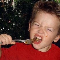 Liten pojke med tufft utseende och gaffel i munnen