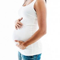 Kvinna i vitt linne och jeans håller om sin gravidmage