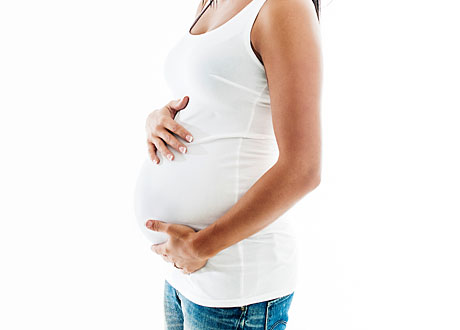 Kvinna i vitt linne och jeans håller om sin gravidmage