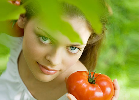Rödhårig ung kvinna i vit blus står i grönska med tomat i handen