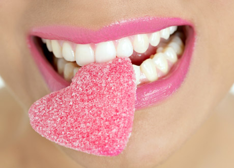 Kvinna med rosa läppar och godishjärta i munnen