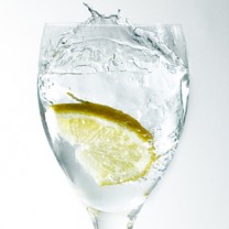 Ett högt glas på fot med citronskiva och vatten som splashar.