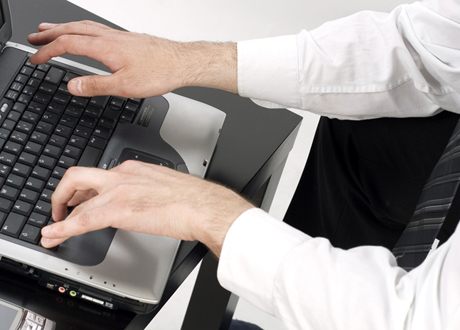 En man i kostym sitter och knappar på sin laptop