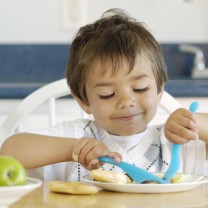 Treårig mörkhårig pojke äter med kniv och gaffel