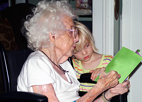 Äldre vithårig kvinna läser med sitt barnbarn