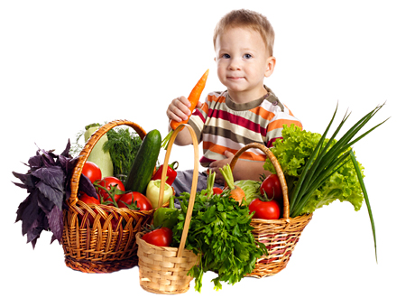 Liten pojke sitter bredvid korg med grönsaker har morot i handen