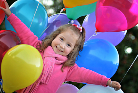 Liten flicka i rosa jacka står i hav av ballonger