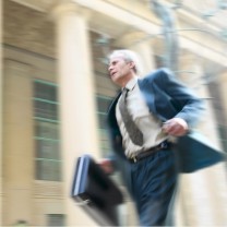 En äldre man i kostym springer stressad med en portfölj