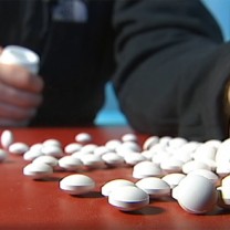 Hand håller i pillerburk piller syns på bord framför handen