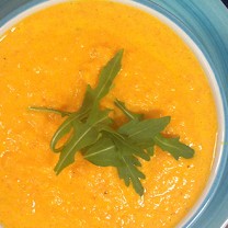 Härligt gul-orange morotssoppa i blå tallrik toppad med ruccola
