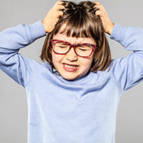 Irriterad ung flicka med glasögon som kliar sig i håret på grund av löss