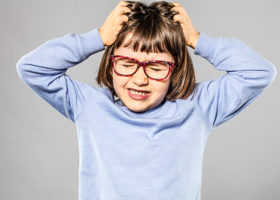 Irriterad ung flicka med glasögon som kliar sig i håret på grund av löss