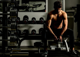 Muskulös man med bar överkropp sitter i gym