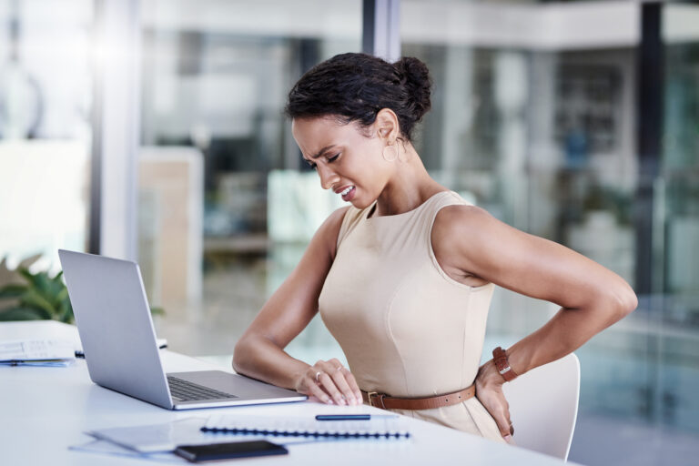 Kvinna vid datorn på jobbet håller sig på värkande ländrygg