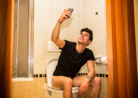 Ung kille sitter på toalett och tar en selfie