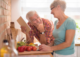 Leende äldre par i köket bland grönsaker