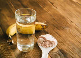 Beige proteinpulver, glas vatten och banan