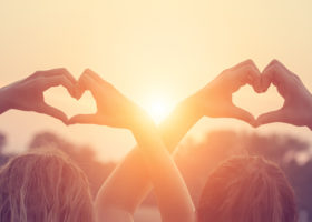 Två hjärtan formas av fyra par händer mot solnedgångsbakgrund