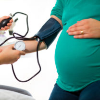 Barn håller blodtrycksmanschett åt sin gravida mamma