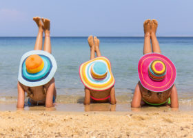 tre kvinnor med solhatt solar vid strandkanten