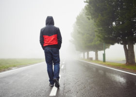 ensam man sedd bakifrån går mitt i väg i regn