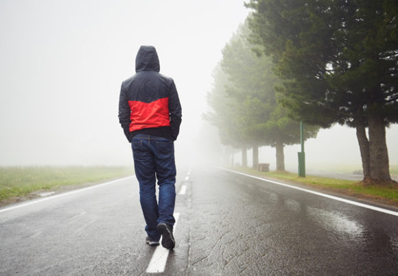 ensam man sedd bakifrån går mitt i väg i regn