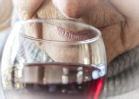 närbild äldre kvinnas mun nära glas med rött vin