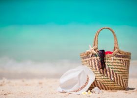 stråväska på stranden med hatt och solglasögon
