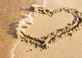 Hjärta ritat i sanden sköljs över med vatten