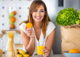 Leende kvinna håller i apelsin och ett glas juice