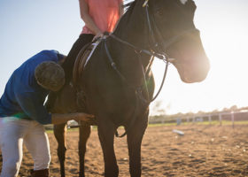 Manlig tränare justerar kvinnas ben i stigbygeln på en på häst
