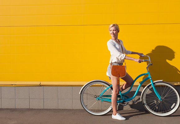 Kvinna som står på en turkos cykel mot en gul vägg