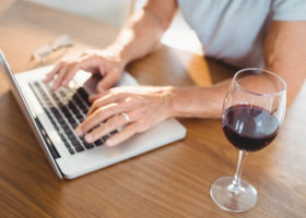 Man skriver på datorn med ett glas rödvin bredvid