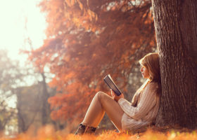 Ung kvinna sitter i en park med fallna höstlöv och läser en bok