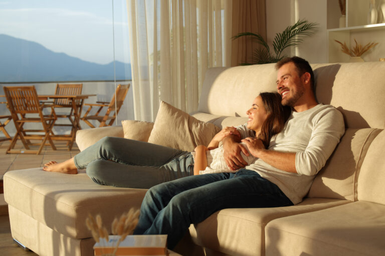 Lyckligt par sitter i soffa i harmoniskt inrett vardagsrum med sjöutsikt