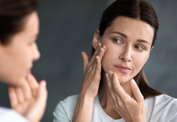 Närbild på olycklig kvinna som tittar på sina hudproblem och akne i spegeln