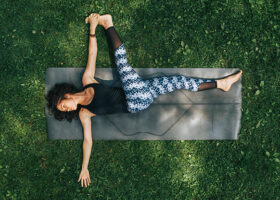 Yogande kvinna gör liggande ryggvridning på yogamatta i gräset